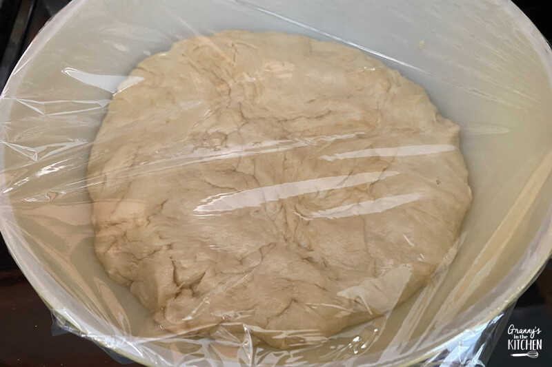 bread dough in bowl with plastic wrap on top