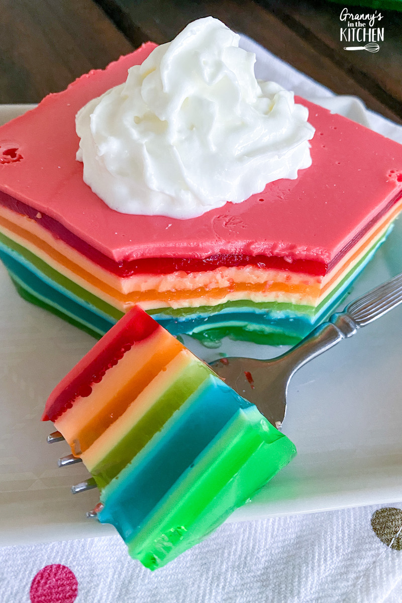layered rainbow jello dessert topped with whipped cream