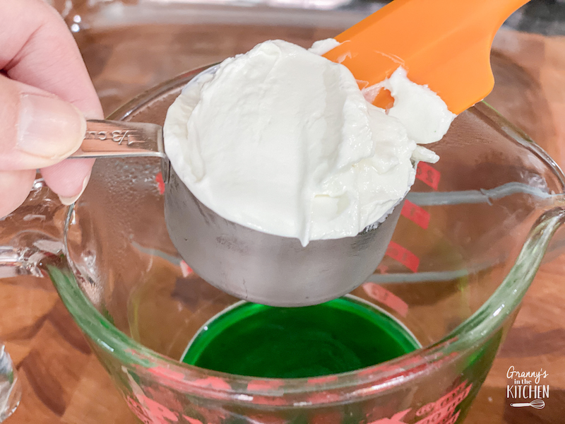adding a scoop of sour cream to green jello liquid