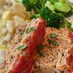 sliced meatloaf on plate with broccoli and potatoes