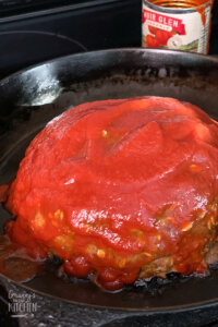 putting tomato sauce on top of meatloaf in iron skillet