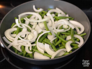 fresh green beans and sliced onions in pan