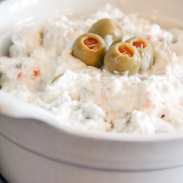 close up of creamy olive dip in a bowl, topped with whole olives