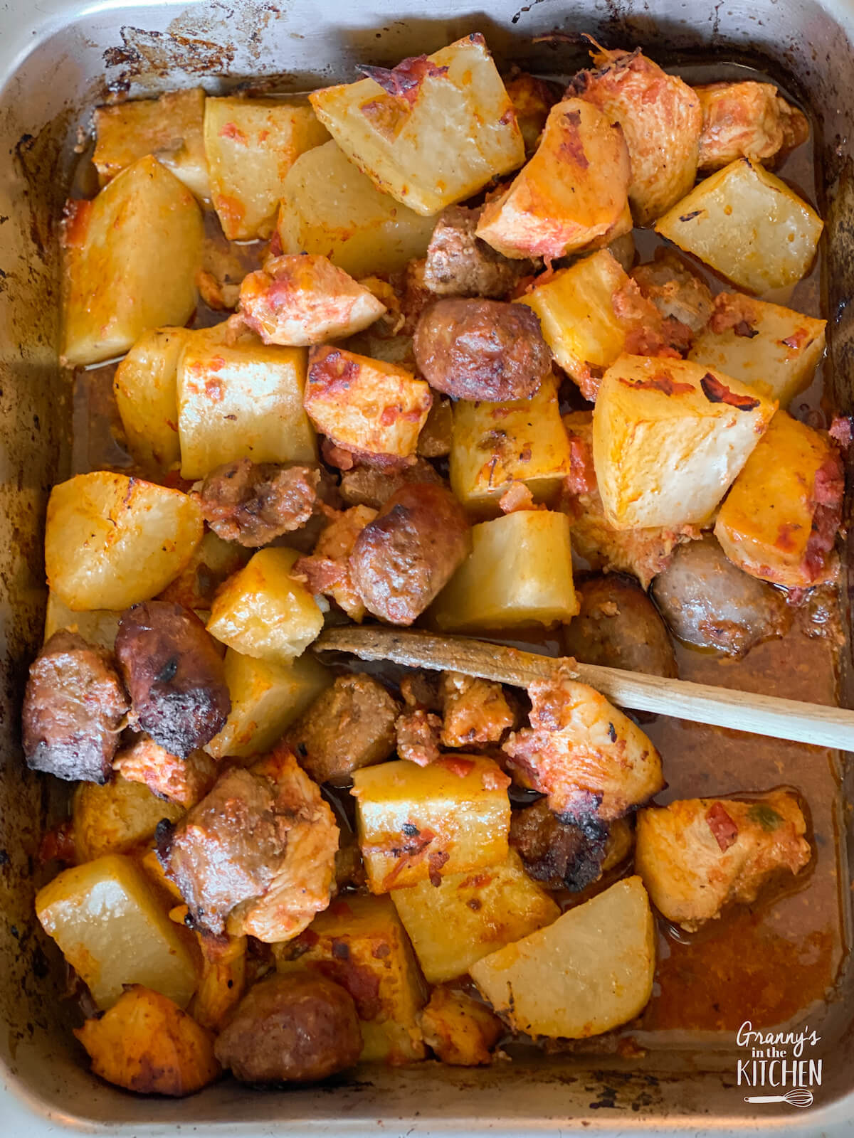stirring roasted chicken, sausage, and potatoes in baking pan