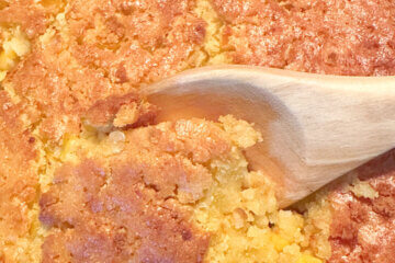 wooden spoon scooping corn casserole from baking dish