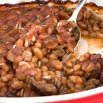 scooping a spoonful of southern style baked beans out of a casserole dish