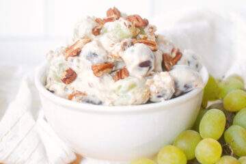 bowl of grape salad on wooden countertop with fresh grapes; text overlay "Creamy Grape Salad"