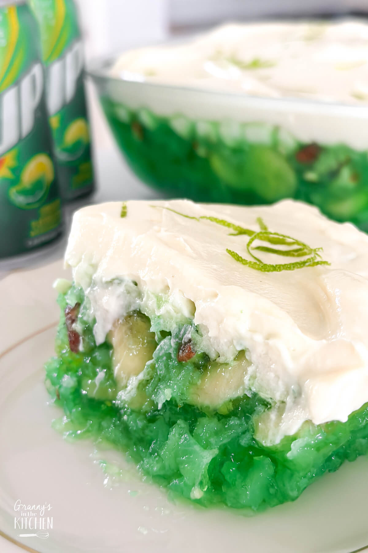 close up of a slice of lime green 7-up jello salad dessert with soda cans in background