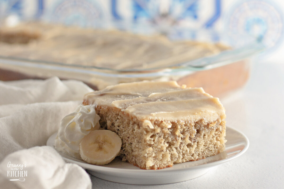 a pan of banana cake in background with a slice in front on a plate