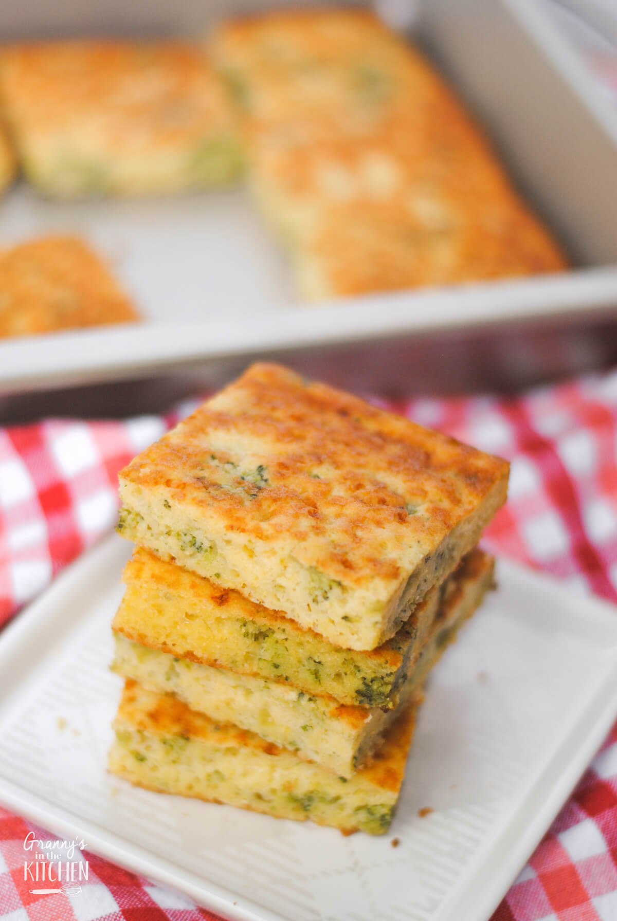 cornbread stacked on a plate, with pan of cornbread in background
