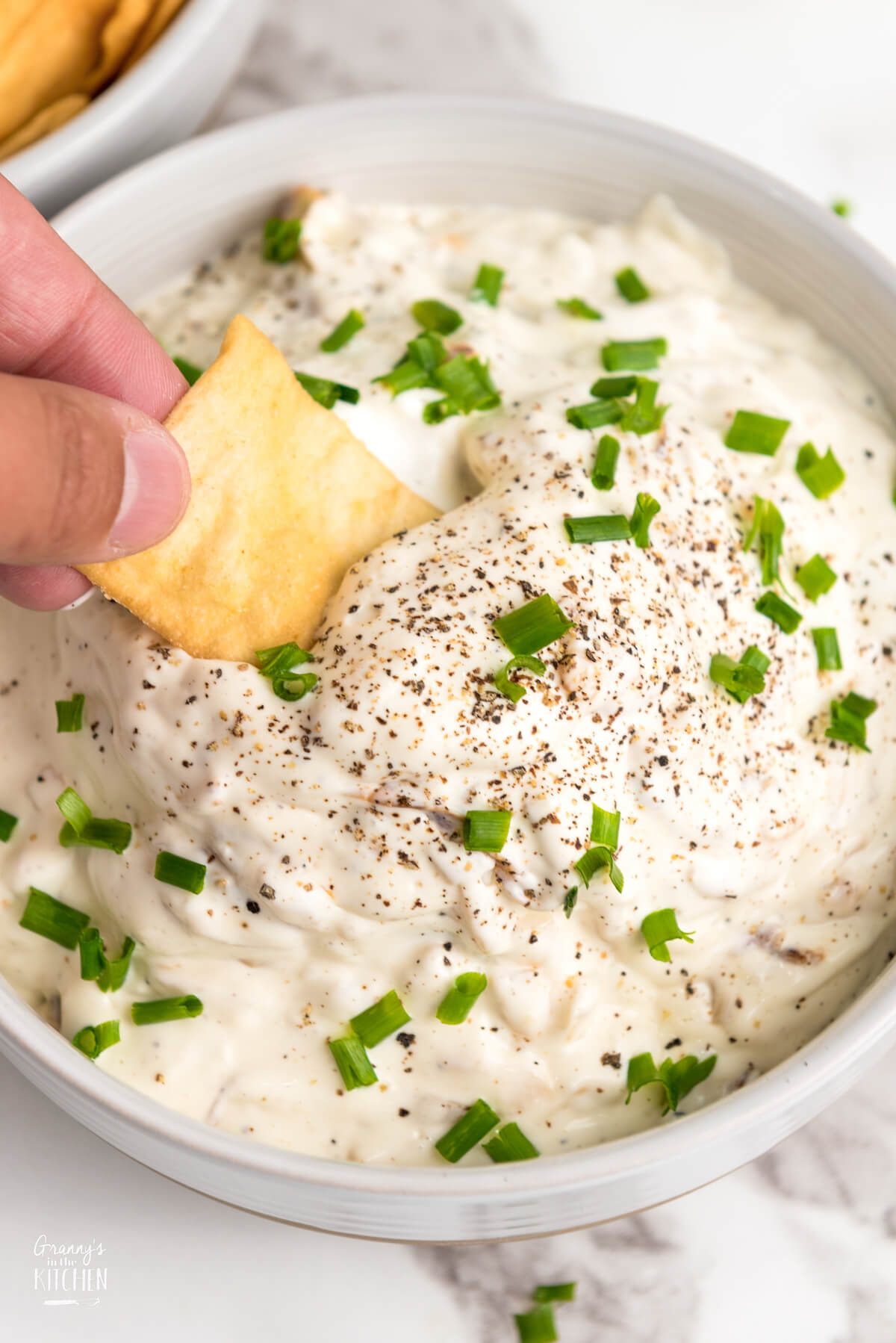dipping a pita chip into a bowl of French Onion dip.