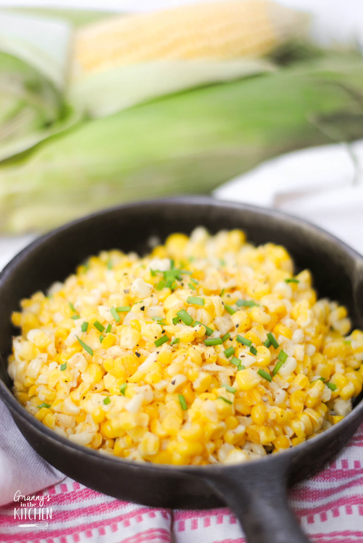 cast iron skillet with fried corn, fresh corn in the background
