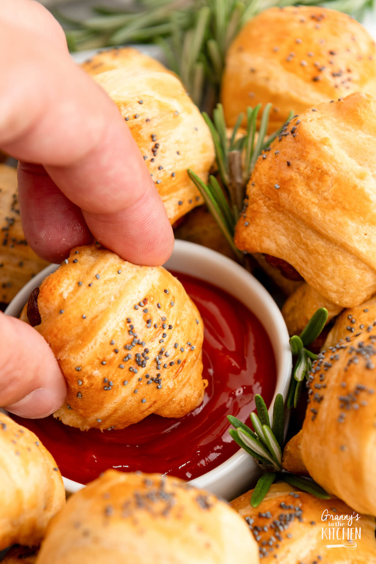 dipping a mini crescent roll pig in a blanket in ketchup