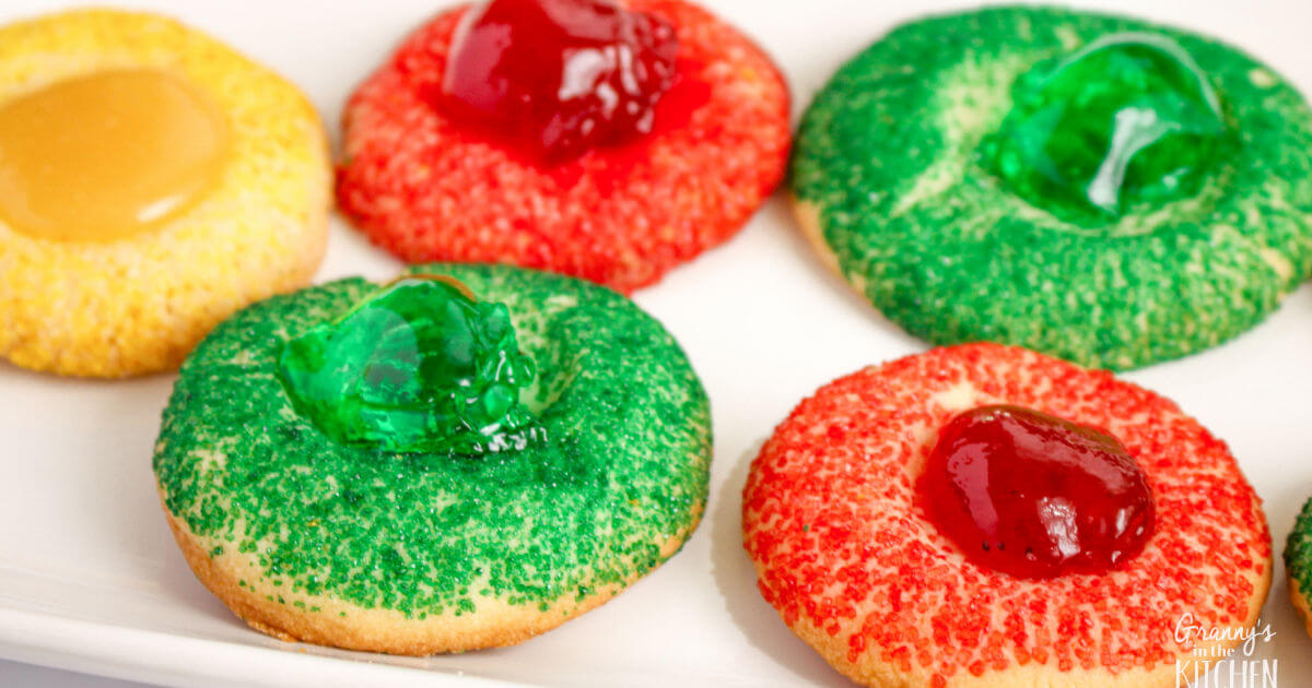 Sanding Sugar Christmas Thumbprint Cookies Thumbprint cookies rolled in red, green and yellow sanding sugar with matching jelly and lemon curd centers on a white plate