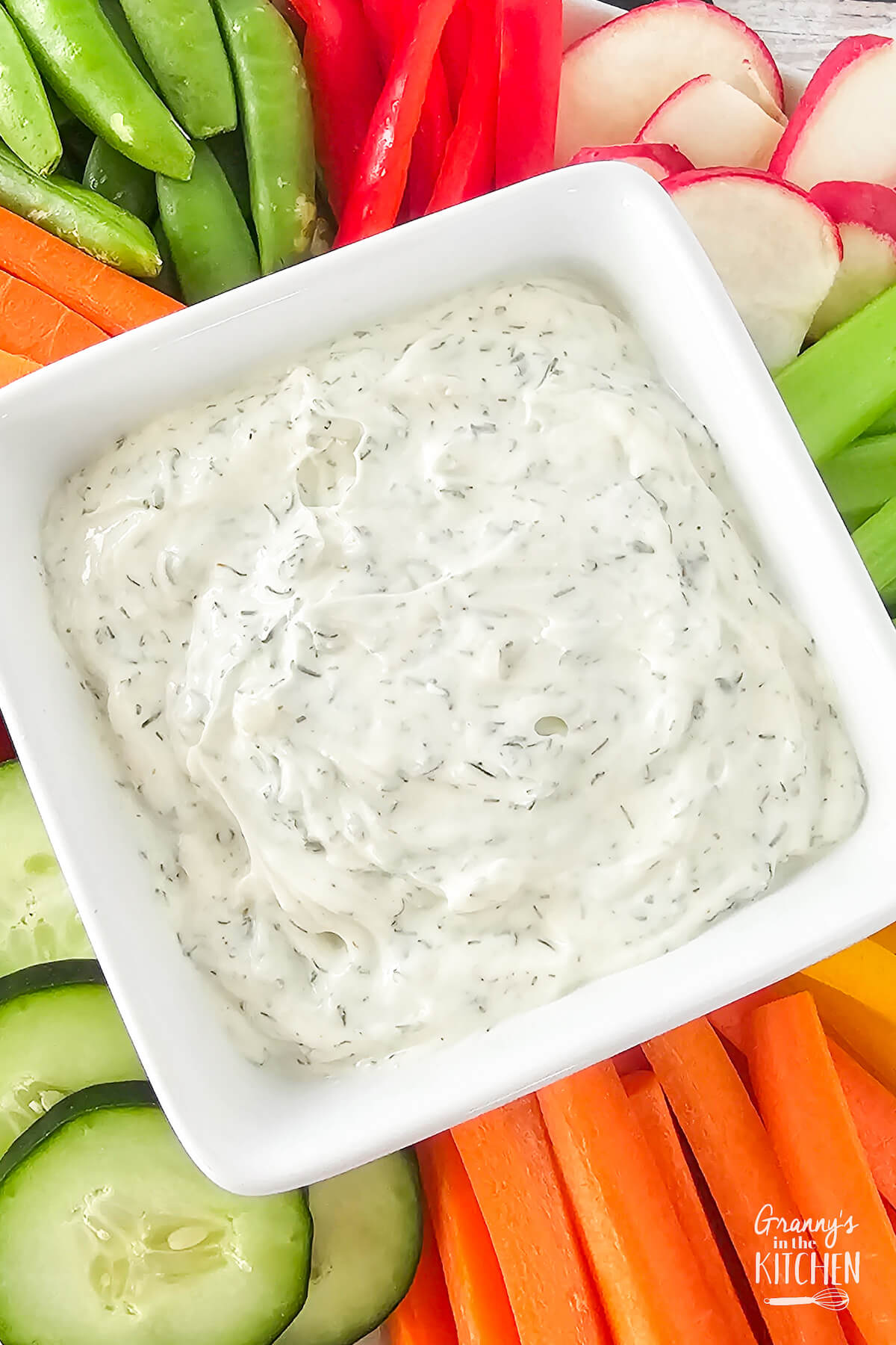 top down view of a bowl of cream dill party dip with fresh veggie slices.