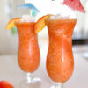 orange frozen drink in hurricane glasses; text overlay "Peach Fuzzy".