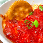 Red pepper cream cheese dip with a cracker dipping into it