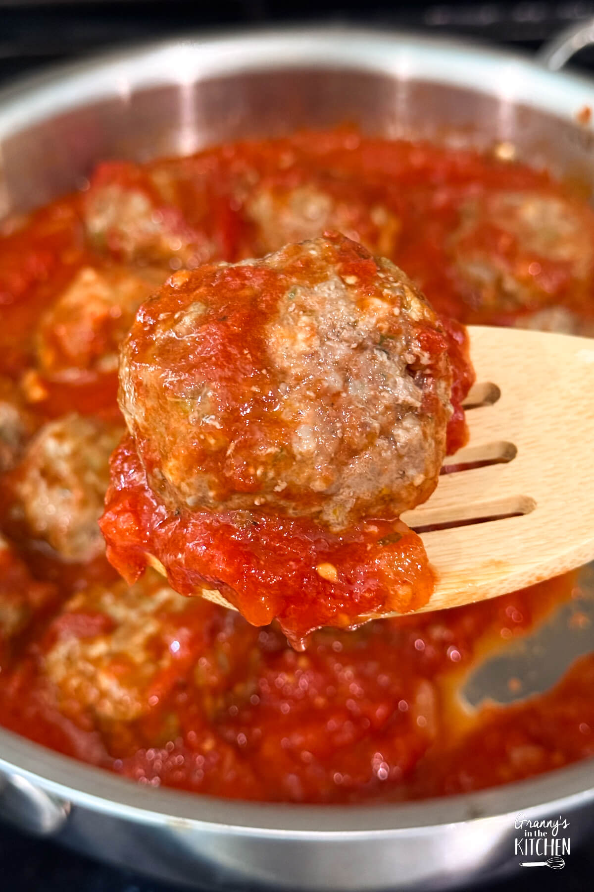 homemade meatball in sauce on a wooden spoon.