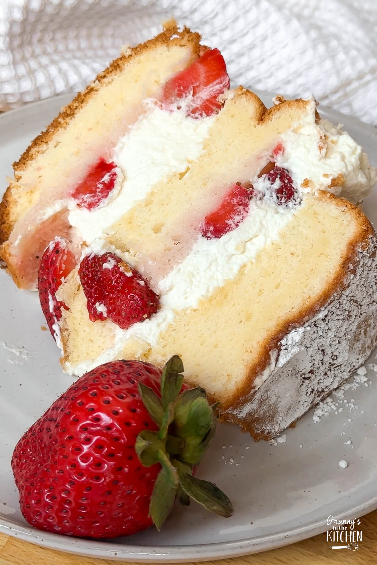close up on a slice of strawberry and cream cake, with fresh strawberries on plate.