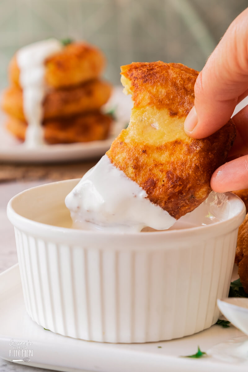 A Potato Fritter being dipped in a white sauce.