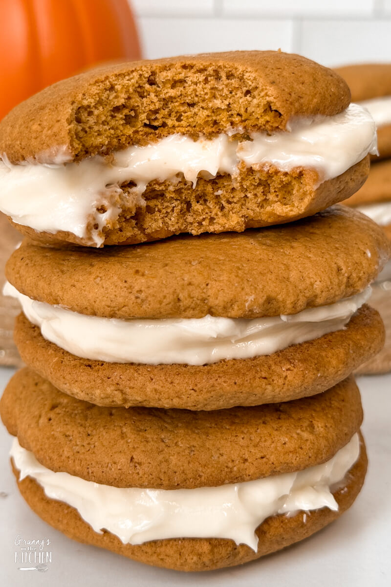 a stack of three homemade pumpkin whoopie pies, the top one with a bite taken.