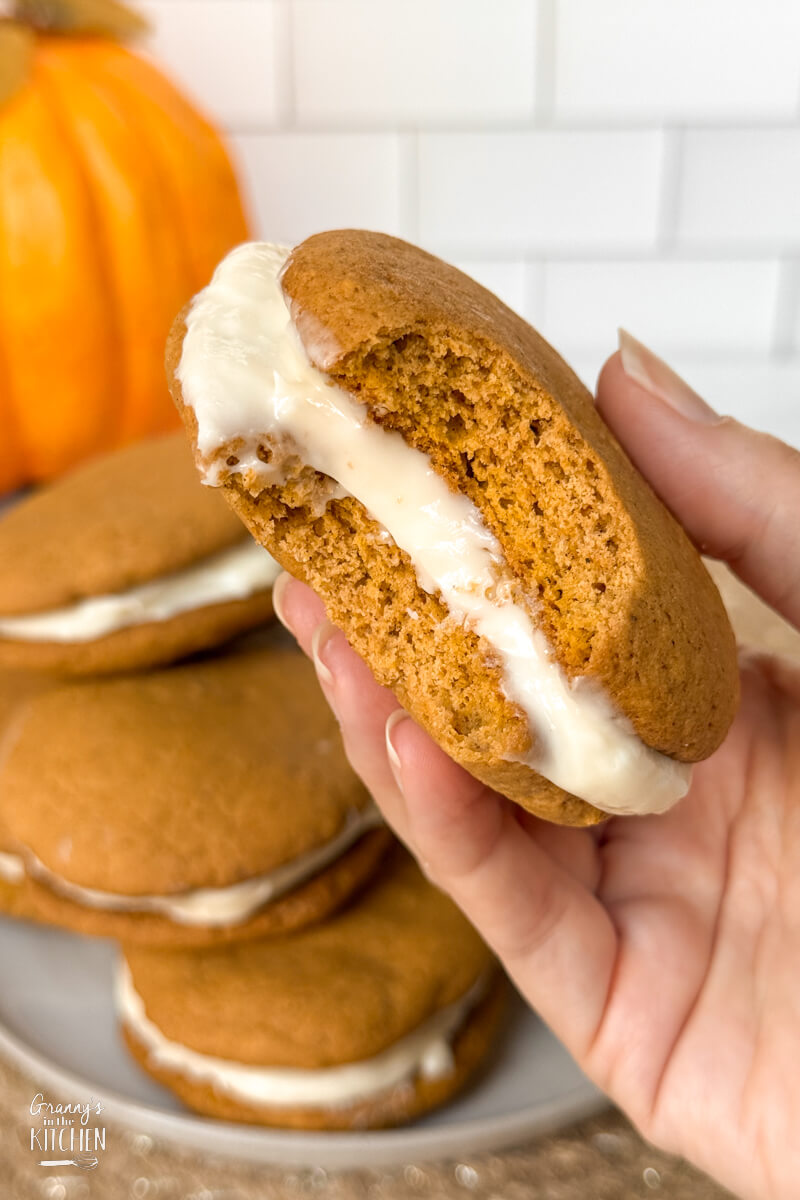 holding a pumpkin whoopie pie with a bite taken.