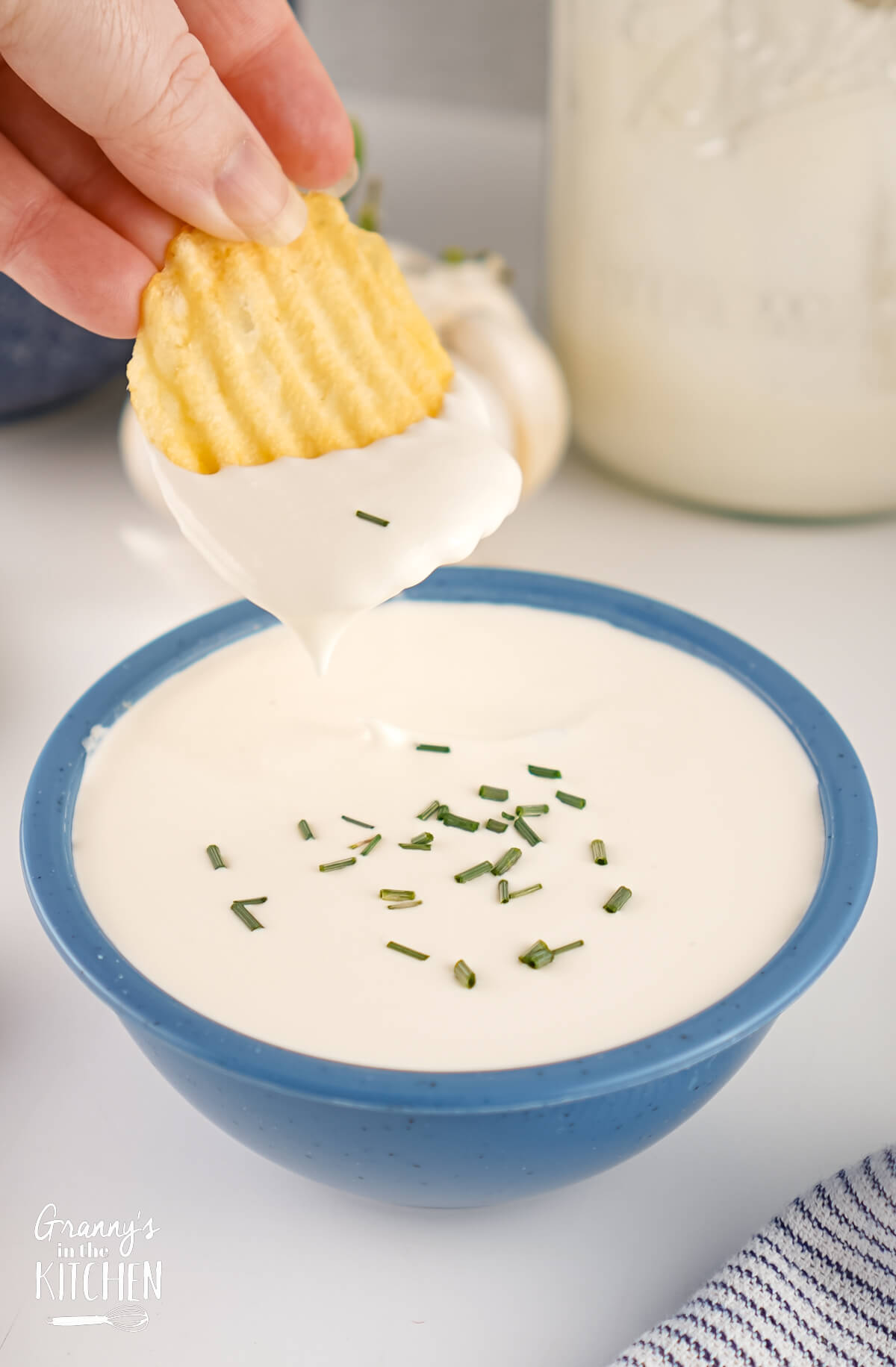 A potato chip being dipped into a bowl of homemade Sour Cream.