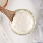 Homemade Sour Cream in a glass jar with a wooden spoon.