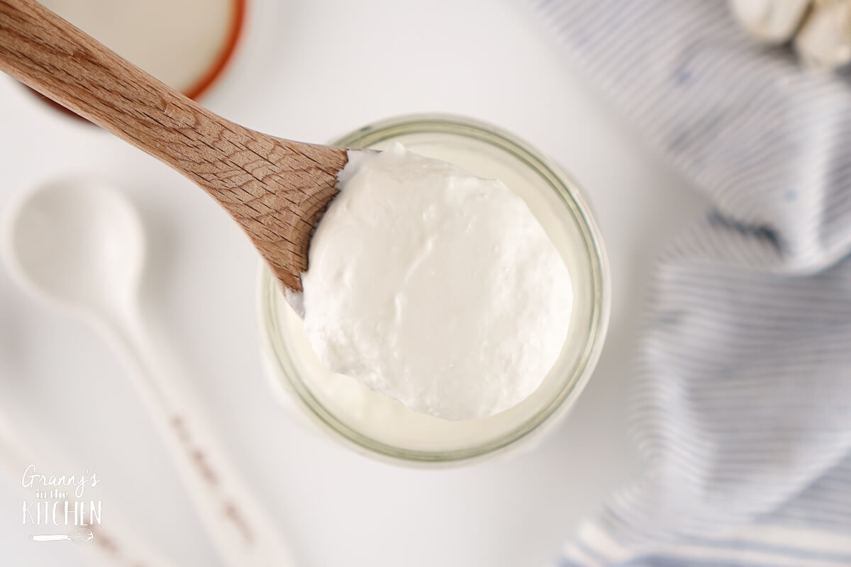 Homemade Sour Cream in a glass jar with a wooden spoon, top-down view.