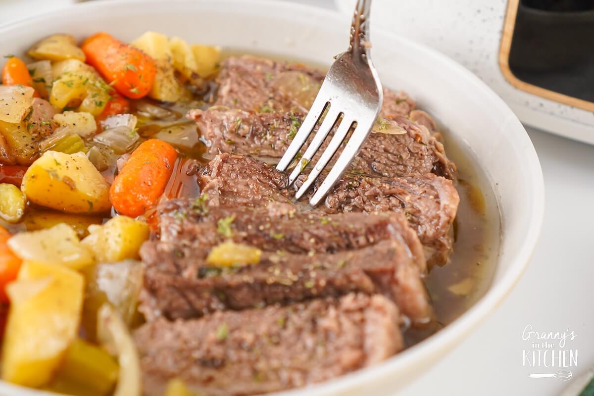 A fork sticking into a plate of pot roast.