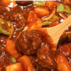 A wooden spoon dipping into sweet and sour meatballs with a text overlay "Sweet and Sour Meatballs."