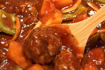 A wooden spoon dipping into sweet and sour meatballs with a text overlay "Sweet and Sour Meatballs."