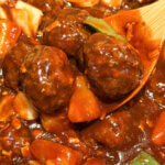 A wooden spoon holding sweet and sour meatballs.