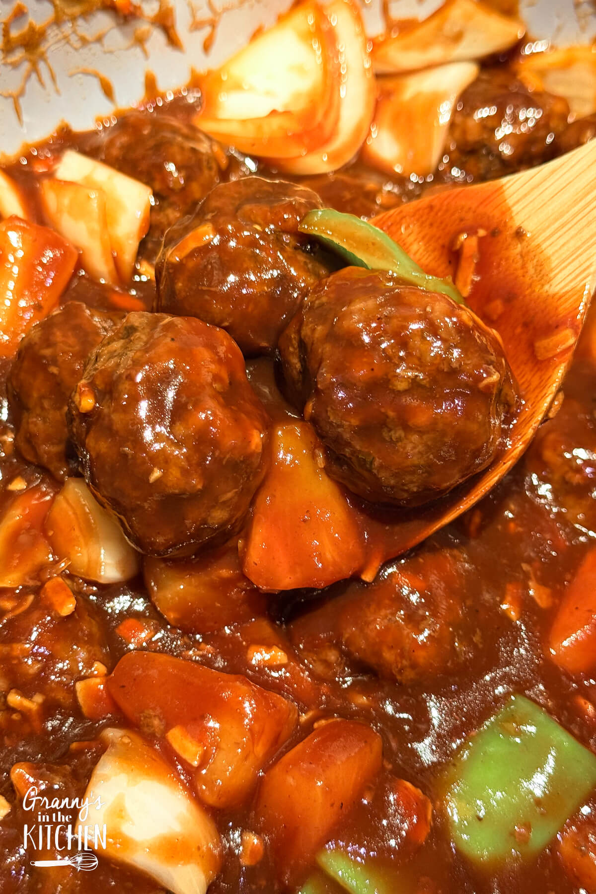 A wooden spoon holding sweet and sour meatballs.