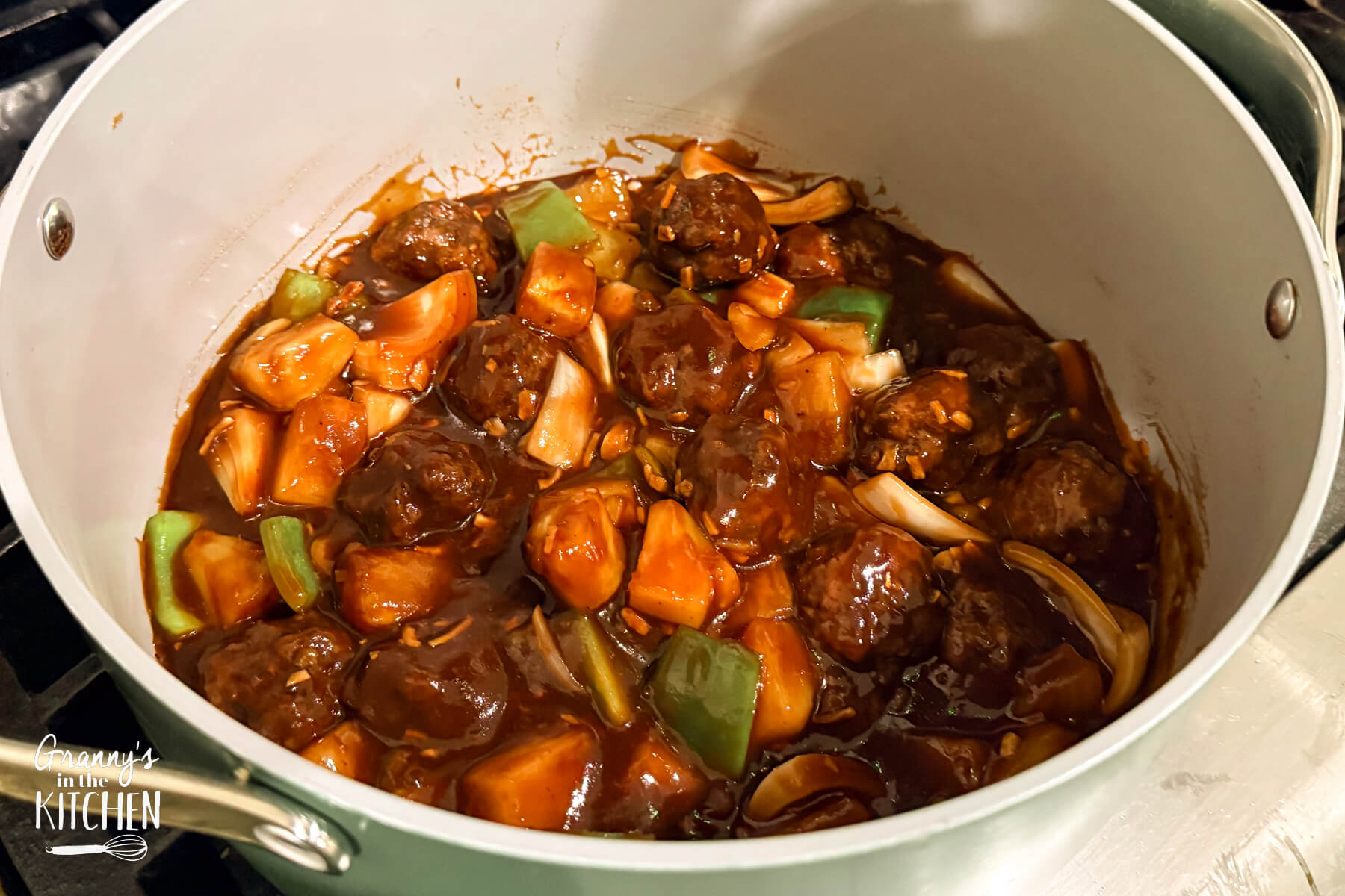 A pot of sweet and sour meatballs on a stove.