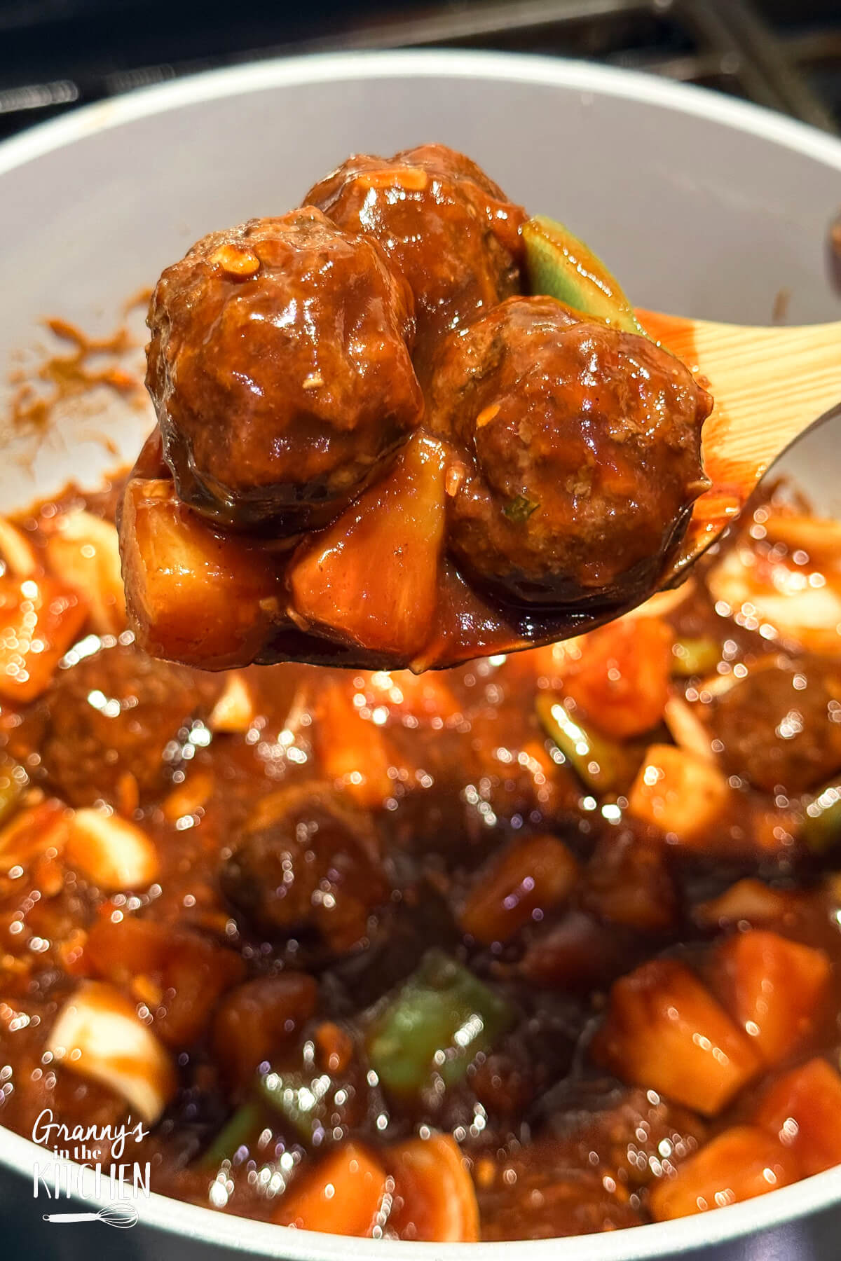 A spoonful of sweet and sour meatballs being held above a full bowl.