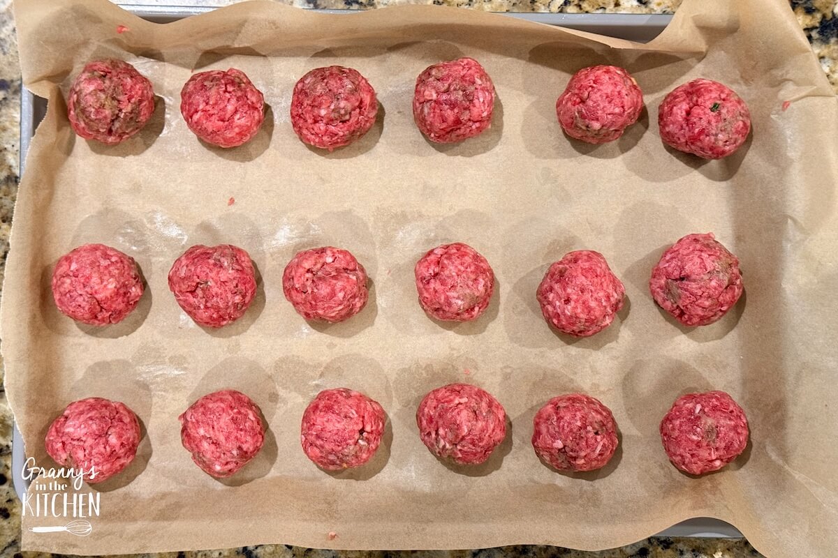 Raw meatballs on a parchment paper lines baking tray.