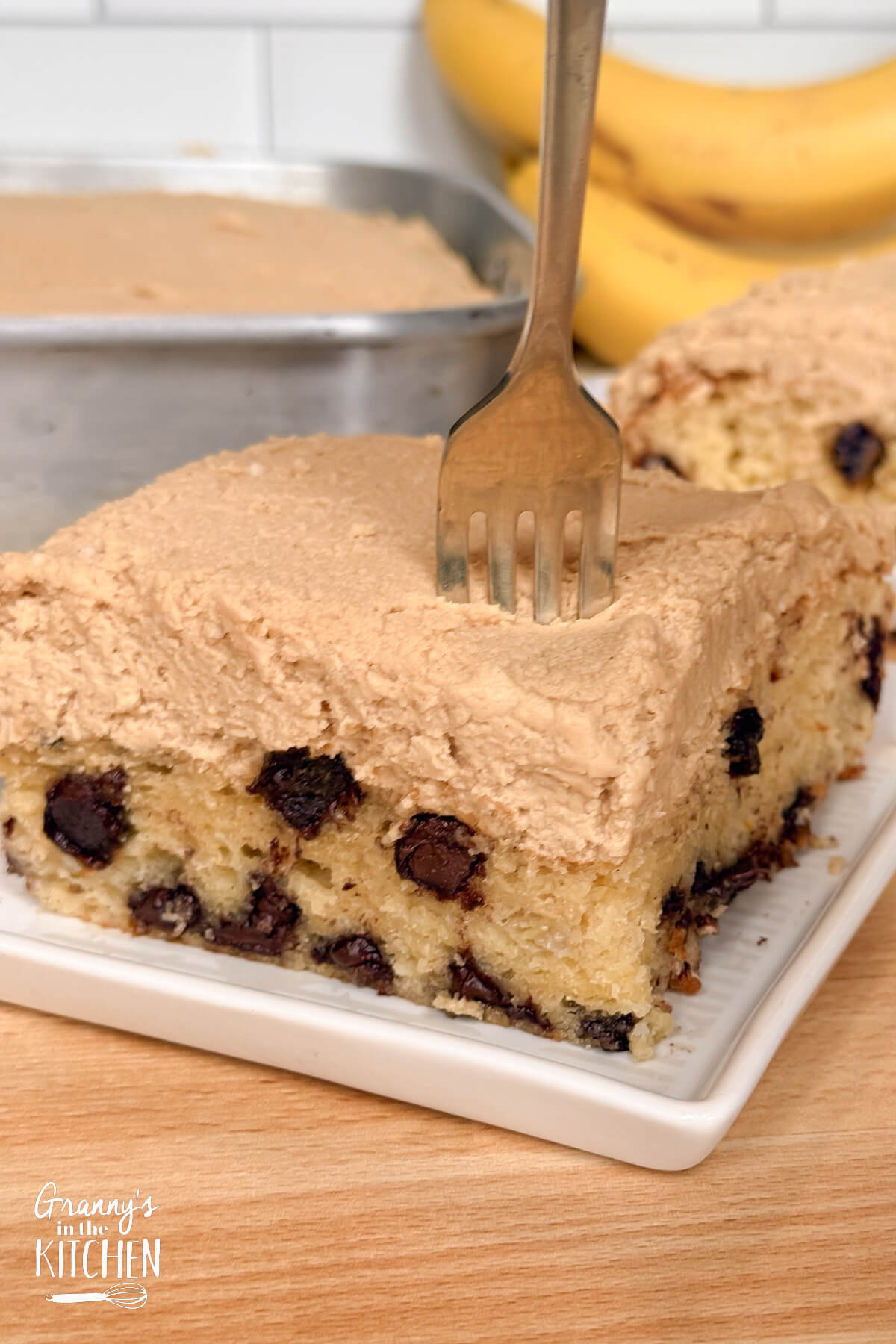 fork cutting a bite of a slice of chocolate chip banana cake.