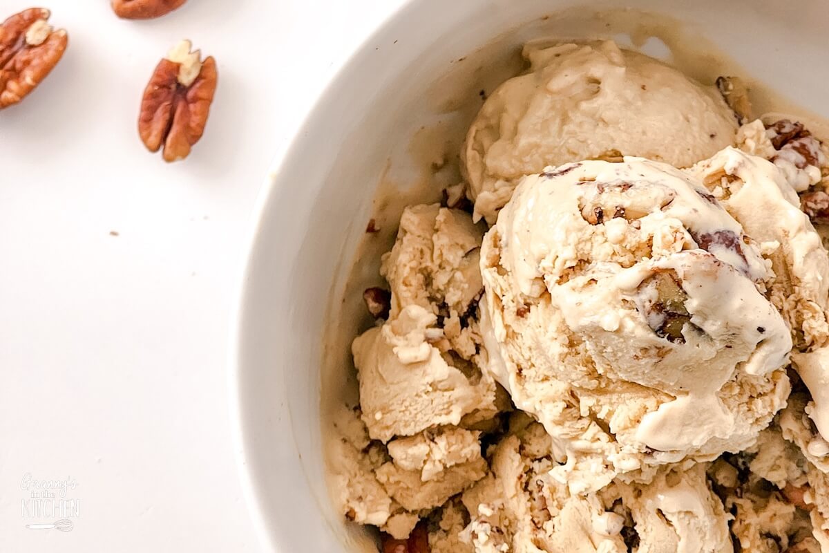 a bowl of homemade butter pecan ice cream with pecan halves next to it.
