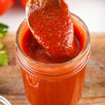 A spoon of Homemade Ketchup being lifted out of a jar.
