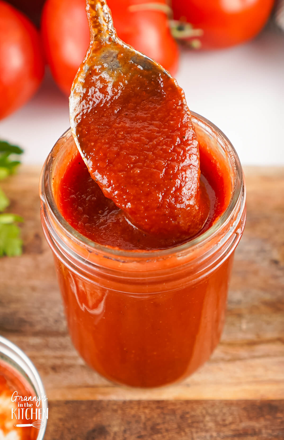 A spoon of Homemade Ketchup being lifted out of a jar.