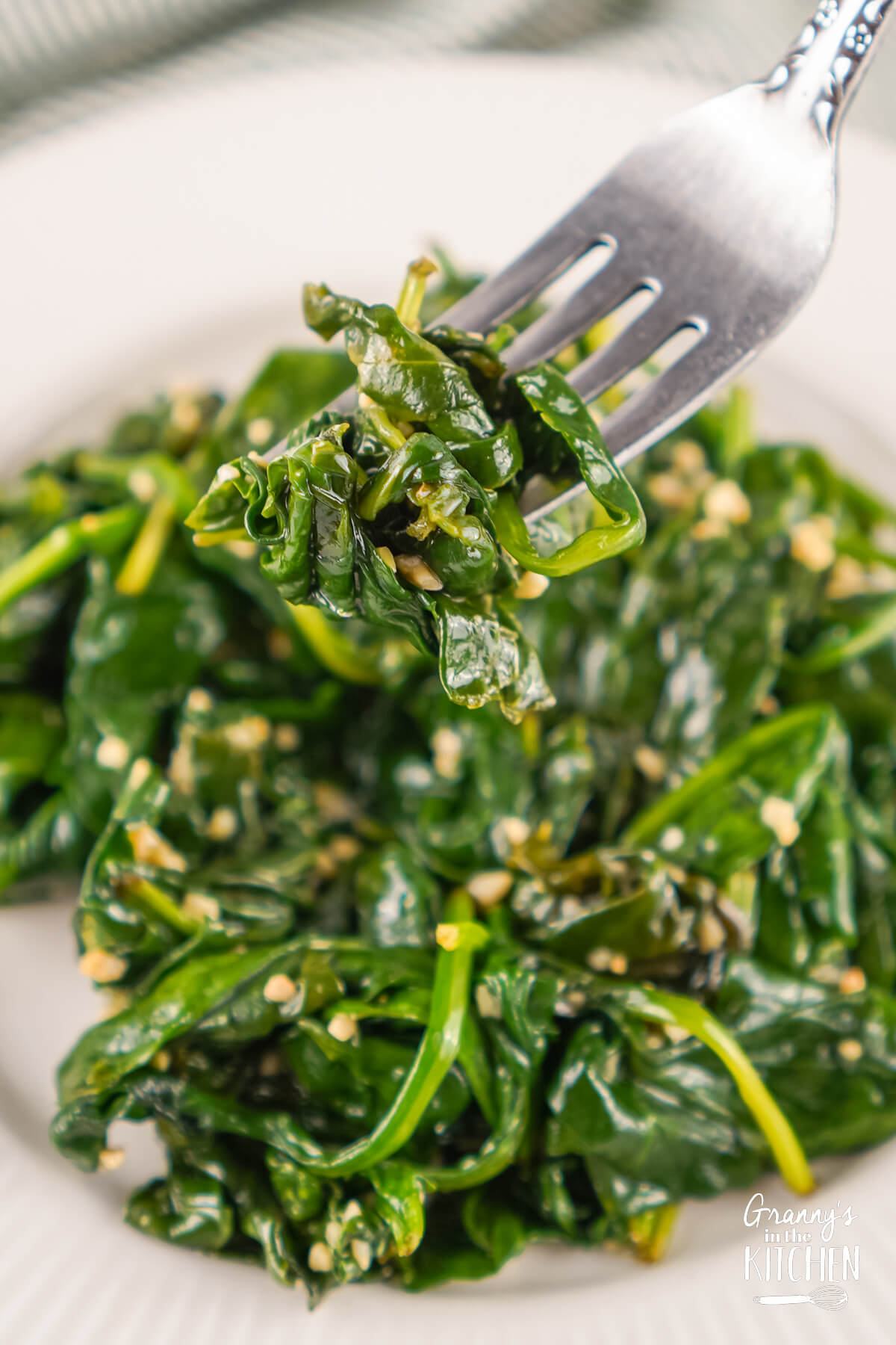 A fork full of Sautéed Spinach being lifted off a plate.