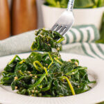 A fork full of Sautéed Spinach being lifted off a plate.